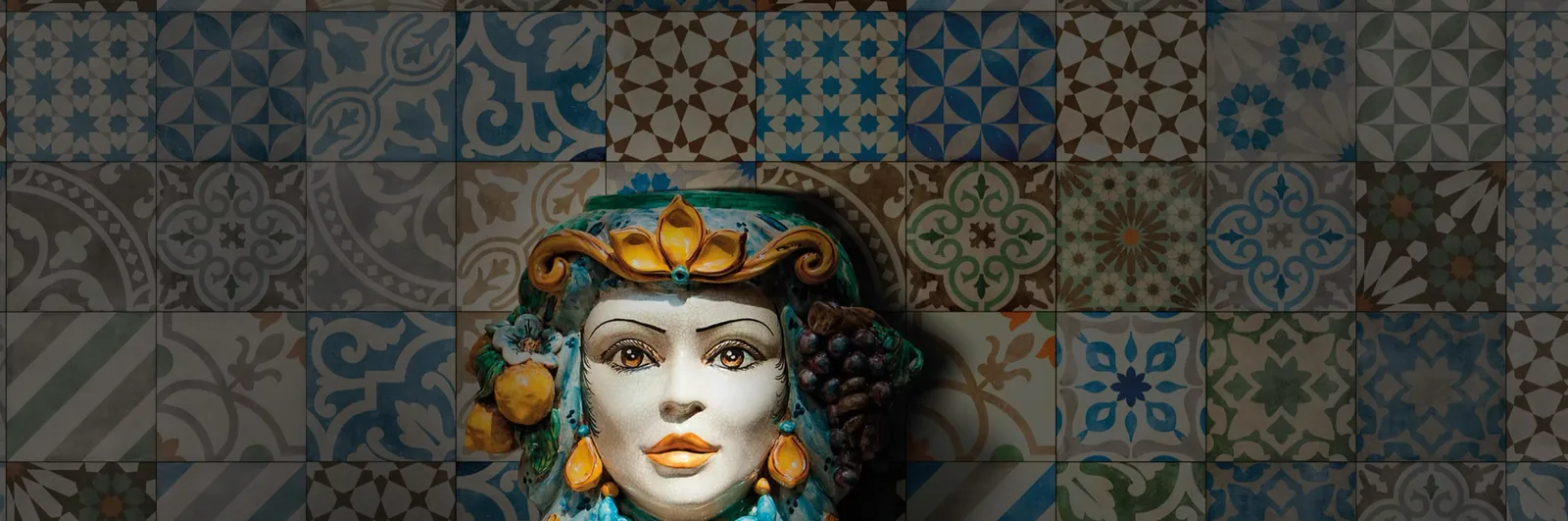 Testa in ceramica della tradizione siciliana davanti a una parete di piastrelle decorate