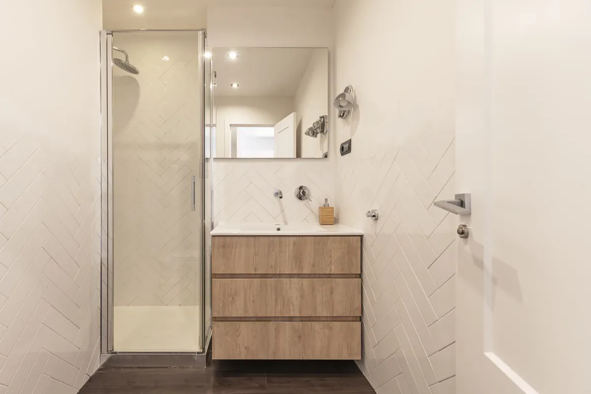 Bagno compatto con box doccia in cristallo, mobile lavabo sospeso e specchio, esempio di come ristrutturare un bagno con budget ridotto