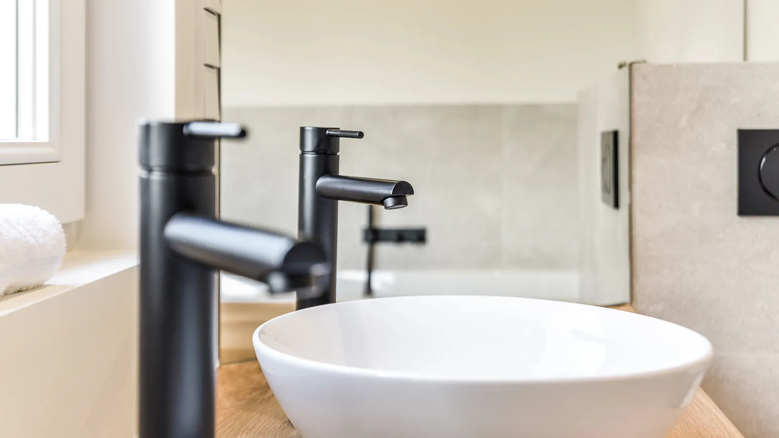 Rubinetti di design in nero opaco, miscelatore alto per lavabo da appoggio in ceramica bianca in un bagno moderno