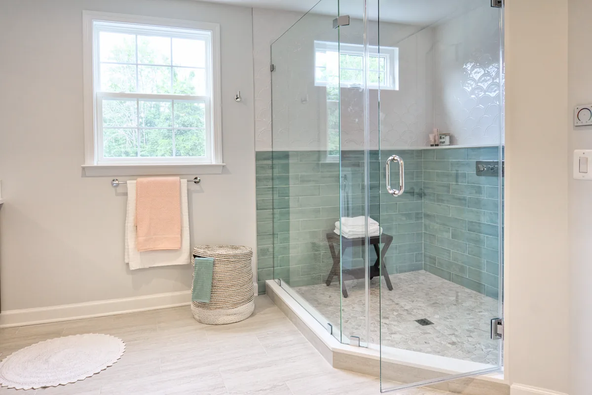 Box doccia in vetro angolare in un bagno piccolo con rivestimento verde e piatto doccia in mosaico